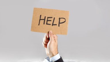 Hand of businessman holding message card asking for help under a pile of papers