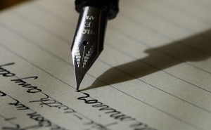 Photo of a caligraphy pen writing words on notepaper